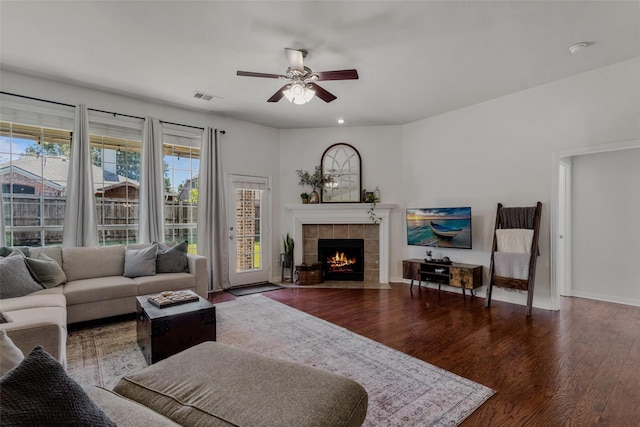 living room featuring ceiling fan, dark wood-type flooring, and a tiled fireplace