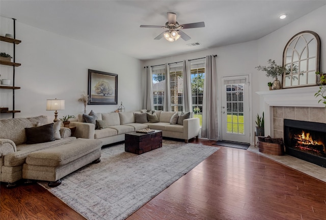 living room with a tiled fireplace, ceiling fan, and dark hardwood / wood-style flooring