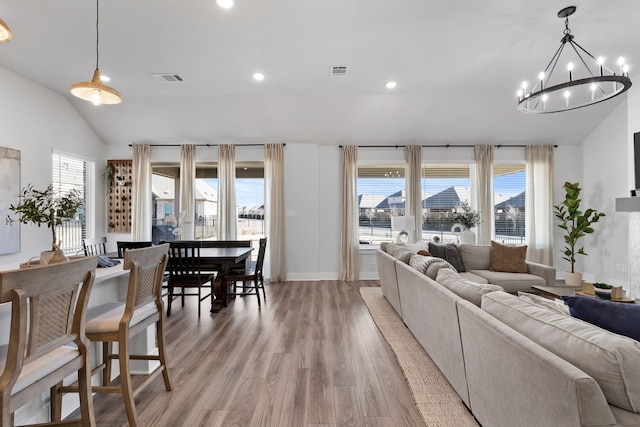 living room with an inviting chandelier, light hardwood / wood-style flooring, and lofted ceiling