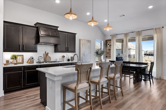 kitchen with decorative light fixtures, lofted ceiling, sink, and an island with sink