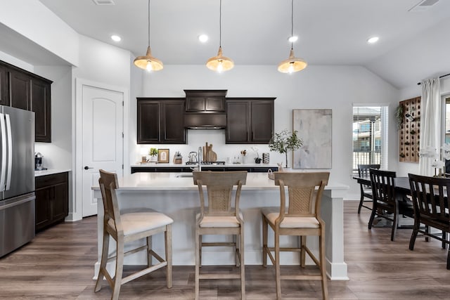 kitchen with decorative light fixtures, an island with sink, stainless steel refrigerator, and vaulted ceiling