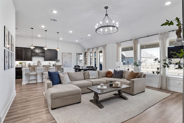 living room with light wood-type flooring, vaulted ceiling, and an inviting chandelier