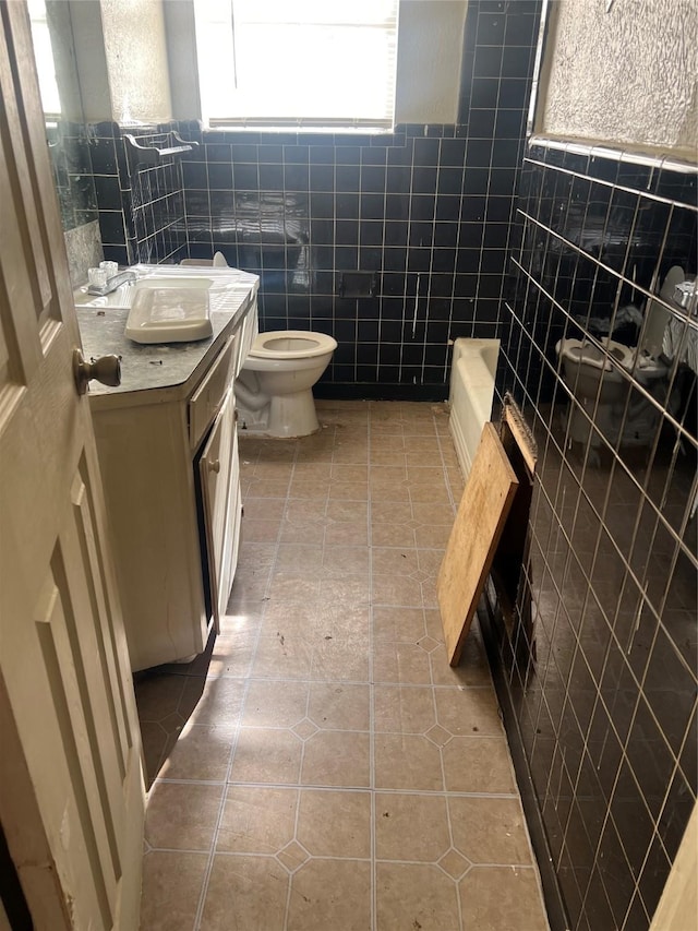 bathroom featuring tile patterned flooring, a bath, toilet, vanity, and tile walls