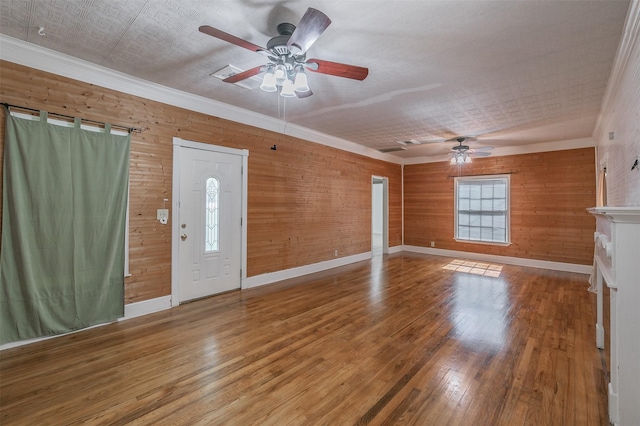 unfurnished living room with wooden walls, hardwood / wood-style floors, ceiling fan, and crown molding