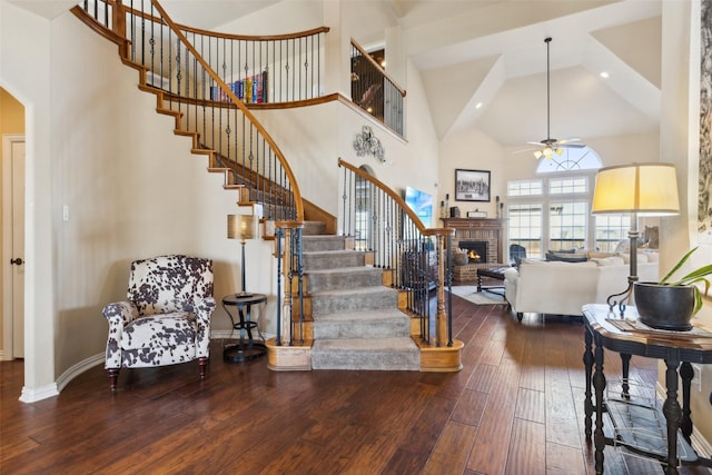 entrance foyer featuring a brick fireplace, ceiling fan, a towering ceiling, and hardwood / wood-style flooring