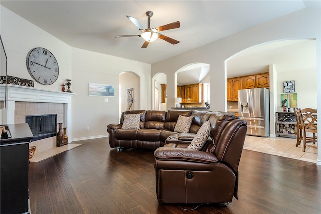 living room with a tile fireplace, light wood-type flooring, and ceiling fan