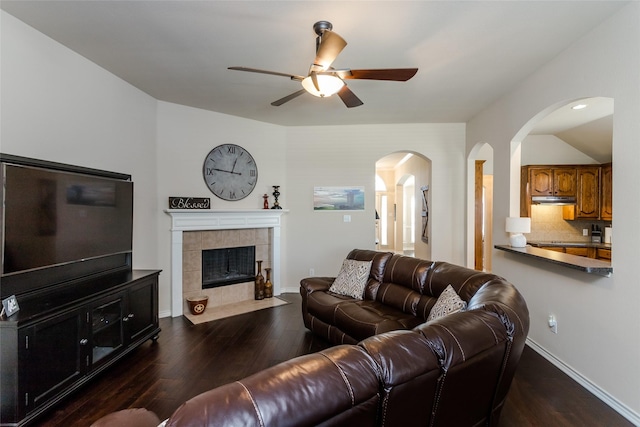 living room featuring ceiling fan, a fireplace, and dark wood-type flooring