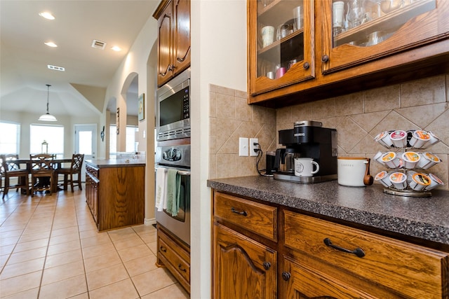 kitchen featuring tasteful backsplash, light tile patterned floors, stainless steel appliances, and decorative light fixtures