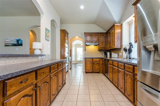 kitchen featuring sink, backsplash, lofted ceiling, light tile patterned floors, and appliances with stainless steel finishes