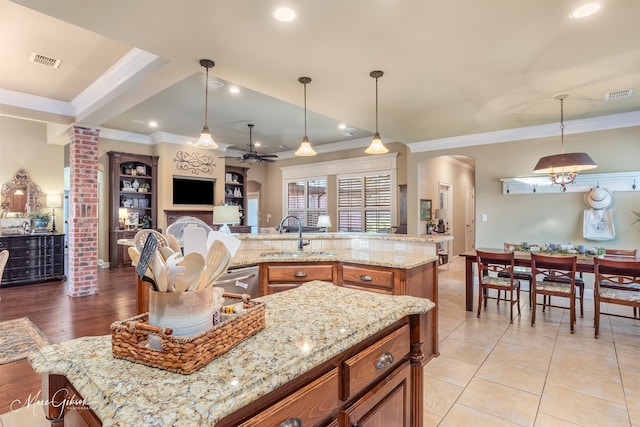 kitchen featuring ceiling fan, a center island, pendant lighting, and light stone counters