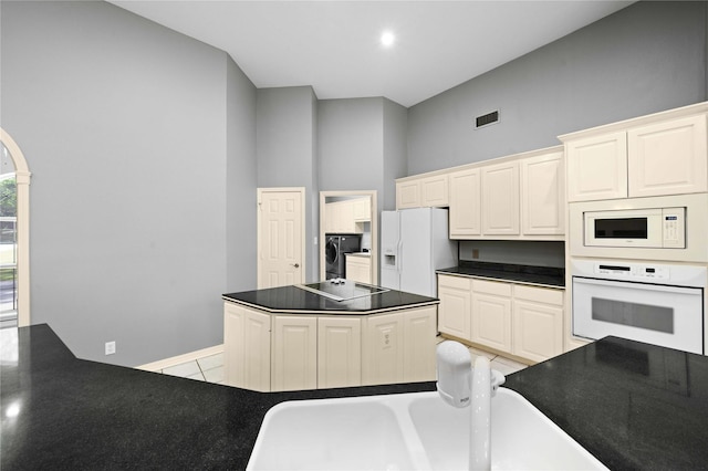 kitchen with white appliances, washer and clothes dryer, light tile patterned floors, a high ceiling, and a center island