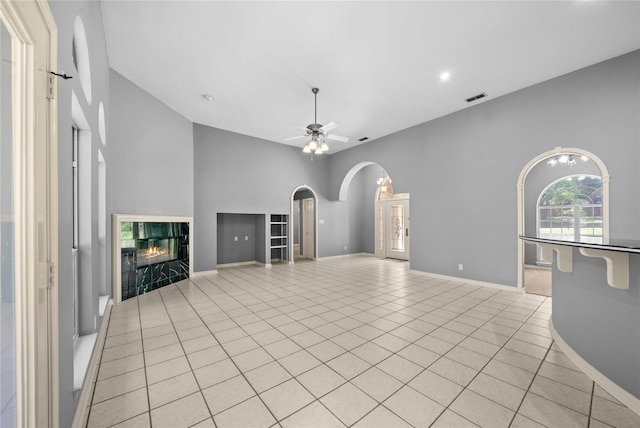 unfurnished living room featuring a towering ceiling, ceiling fan, a fireplace, and light tile patterned floors