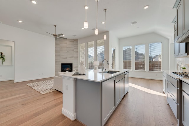 kitchen with ceiling fan, pendant lighting, a fireplace, gray cabinets, and an island with sink