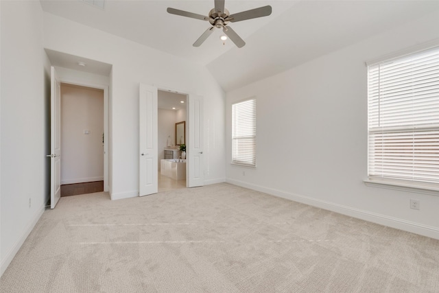 unfurnished bedroom with ceiling fan, lofted ceiling, connected bathroom, and multiple windows