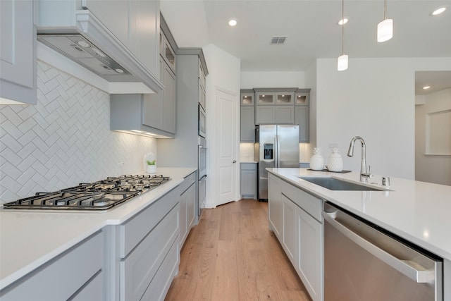 kitchen with light wood-type flooring, tasteful backsplash, stainless steel appliances, sink, and pendant lighting