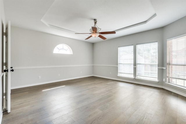 empty room with hardwood / wood-style floors, ceiling fan, a healthy amount of sunlight, and a raised ceiling