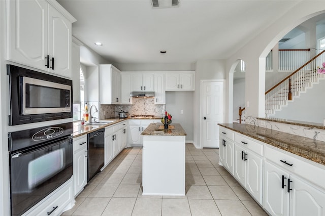 kitchen featuring dark stone counters, sink, black appliances, a center island, and white cabinetry