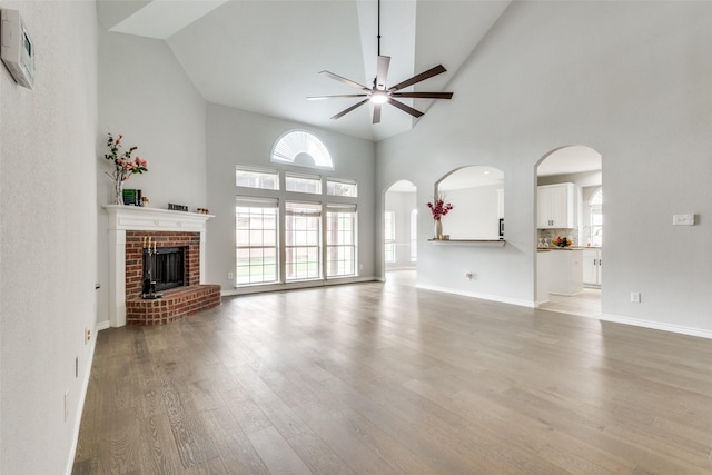 unfurnished living room featuring a fireplace, a high ceiling, light hardwood / wood-style floors, and ceiling fan