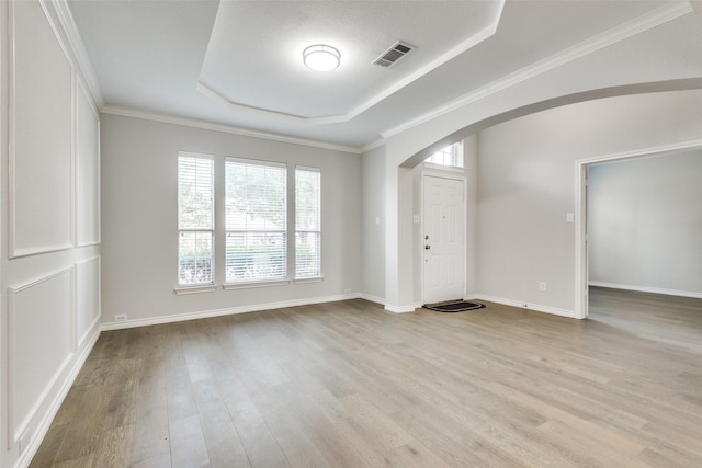 empty room featuring a raised ceiling, light hardwood / wood-style floors, and a textured ceiling