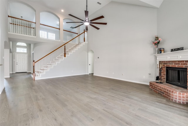 unfurnished living room with ceiling fan, high vaulted ceiling, light hardwood / wood-style floors, and a brick fireplace