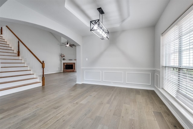 unfurnished dining area featuring a raised ceiling, light hardwood / wood-style flooring, a brick fireplace, and ceiling fan