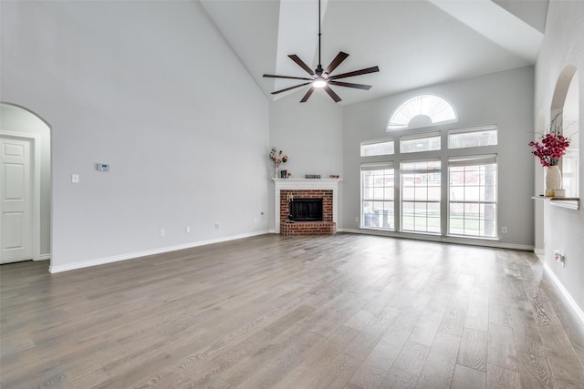 unfurnished living room with a fireplace, a high ceiling, light wood-type flooring, and ceiling fan