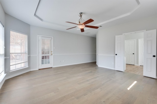 empty room with ceiling fan, a raised ceiling, and light hardwood / wood-style flooring