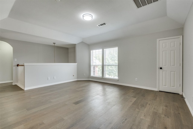 empty room featuring hardwood / wood-style flooring, a raised ceiling, and lofted ceiling