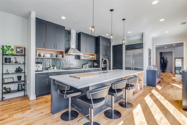 kitchen with a breakfast bar area, hanging light fixtures, wall chimney exhaust hood, and an island with sink