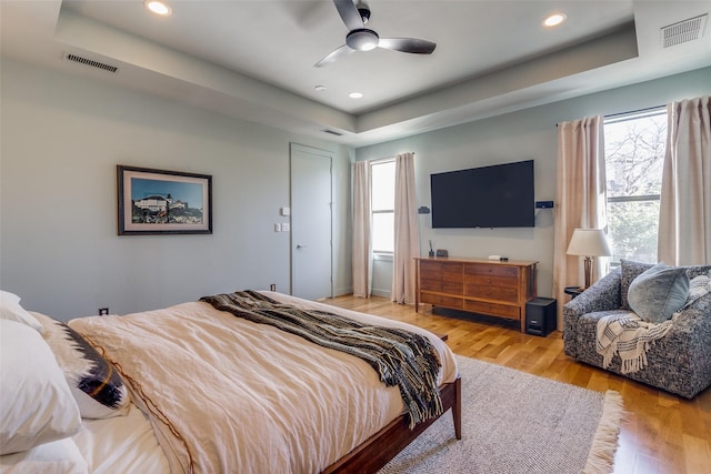 bedroom with a raised ceiling, ceiling fan, and light hardwood / wood-style floors