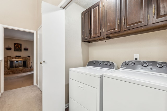 clothes washing area featuring a fireplace, light carpet, washer and dryer, and cabinets