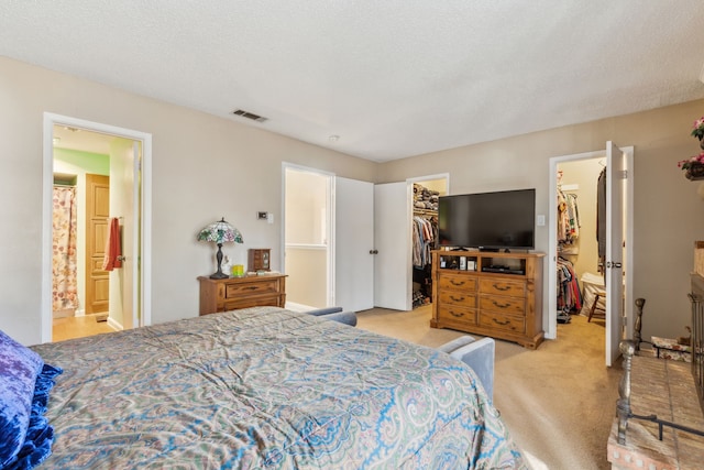 bedroom with light carpet, ensuite bathroom, a textured ceiling, a spacious closet, and a closet