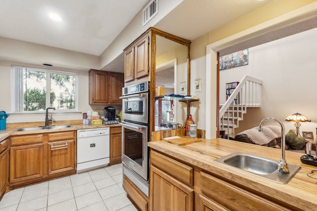 kitchen with dishwasher, stainless steel double oven, sink, and light tile patterned floors