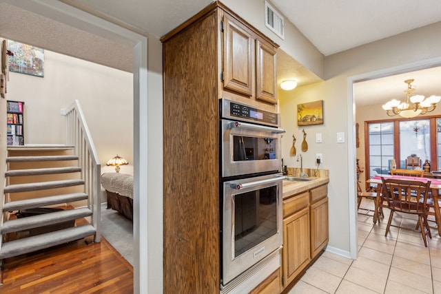 kitchen featuring pendant lighting, sink, light tile patterned floors, double oven, and a chandelier