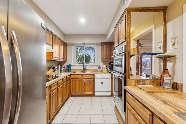 9728 Amberton Pkwy, Dallas, TX 75243 - kitchen with appliances with stainless steel finishes, a sink, under cabinet range hood, light tile patterned floors, and brown cabinets