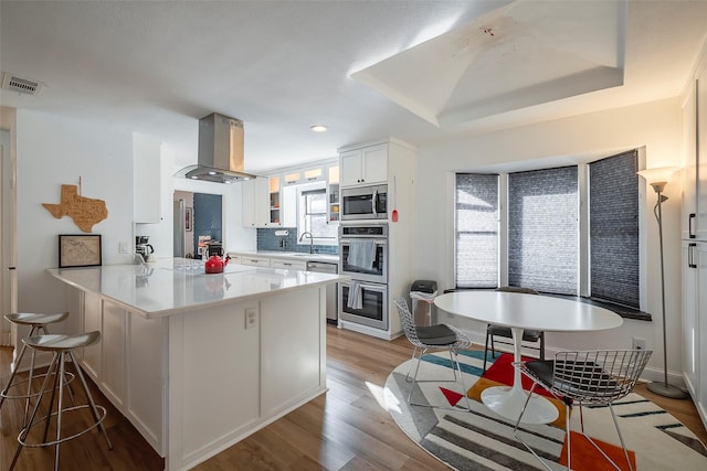 kitchen featuring sink, stainless steel appliances, kitchen peninsula, island range hood, and white cabinets