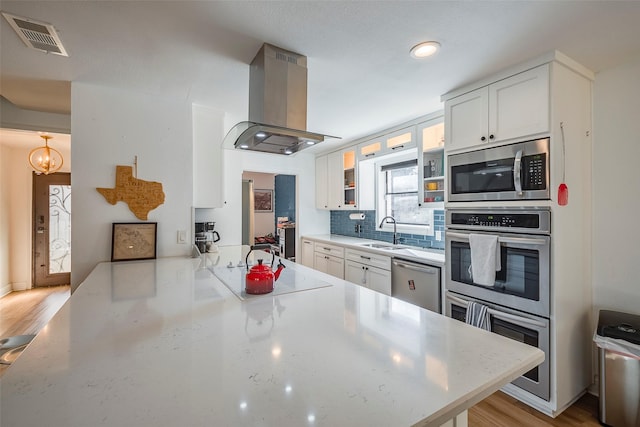 kitchen featuring sink, white cabinetry, island range hood, kitchen peninsula, and stainless steel appliances