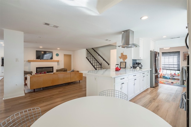 kitchen with white cabinetry, island exhaust hood, stainless steel fridge, and light wood-type flooring