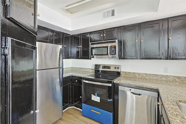 kitchen with light hardwood / wood-style floors, light stone countertops, and stainless steel appliances