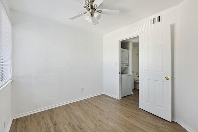 unfurnished bedroom featuring ceiling fan, light hardwood / wood-style flooring, and stacked washing maching and dryer