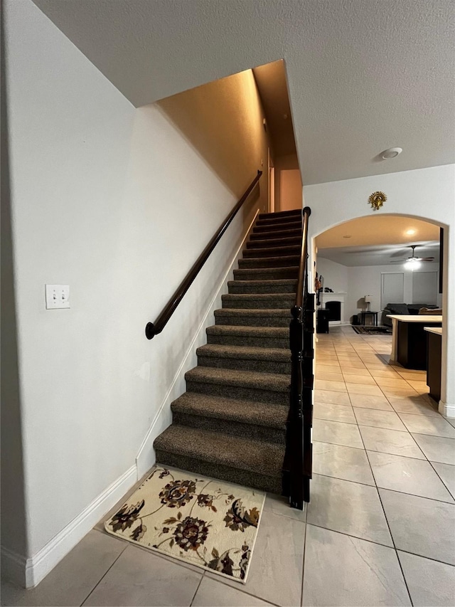 stairs featuring tile patterned flooring, a textured ceiling, and ceiling fan