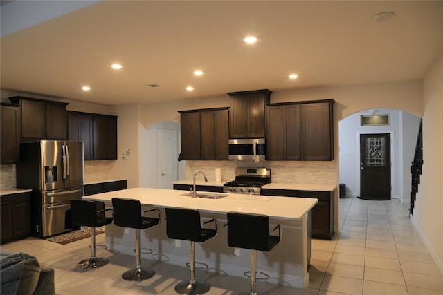 kitchen with dark brown cabinets, stainless steel appliances, sink, a center island with sink, and light tile patterned flooring