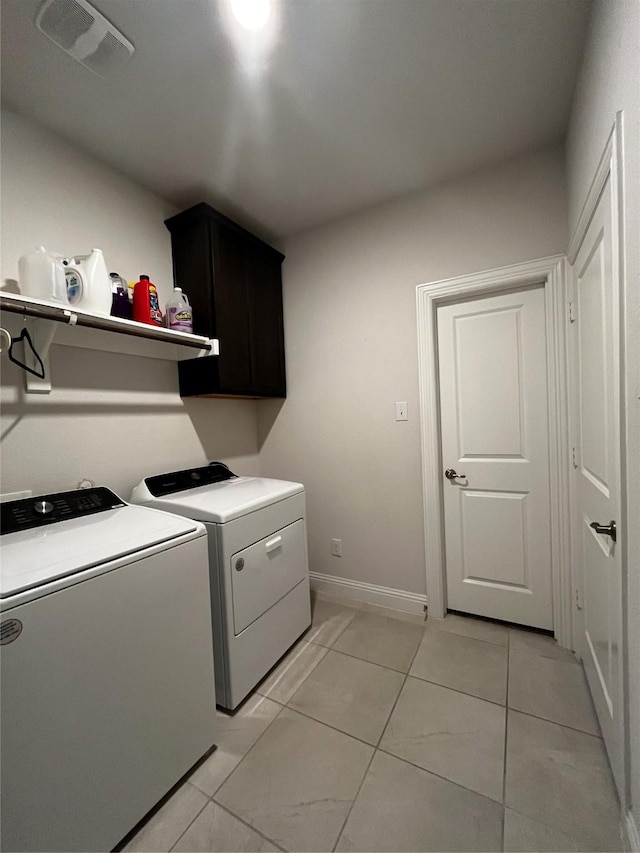 clothes washing area with cabinets, light tile patterned floors, and washer and clothes dryer