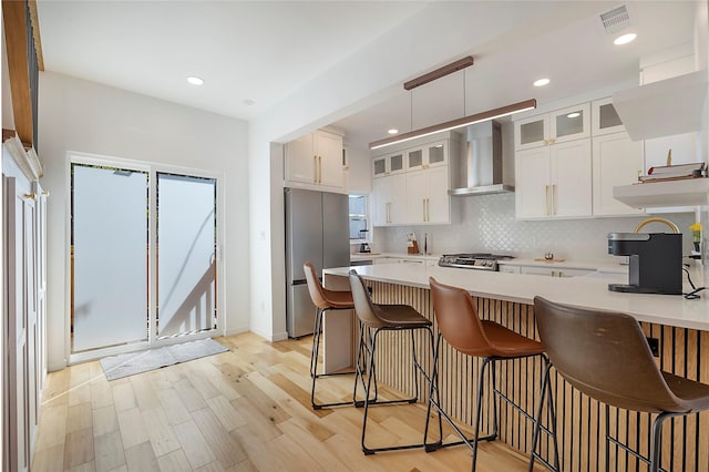 kitchen featuring wall chimney range hood, backsplash, stainless steel fridge, white cabinets, and light wood-type flooring