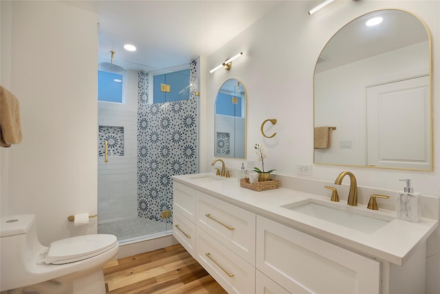 bathroom featuring hardwood / wood-style flooring, toilet, vanity, and tiled shower