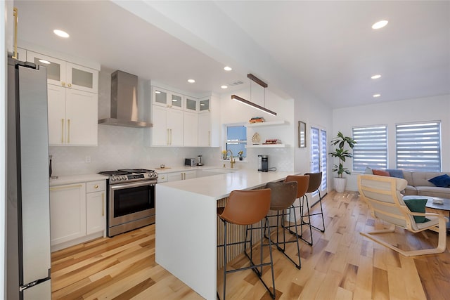 kitchen with appliances with stainless steel finishes, light hardwood / wood-style floors, white cabinetry, and wall chimney exhaust hood