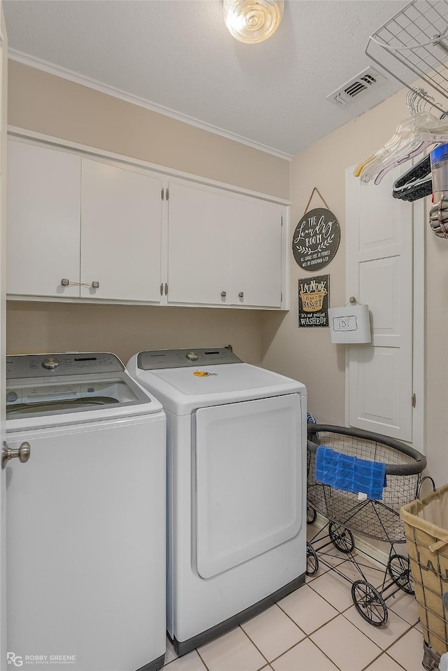 clothes washing area with cabinets, light tile patterned floors, washer and clothes dryer, and ornamental molding