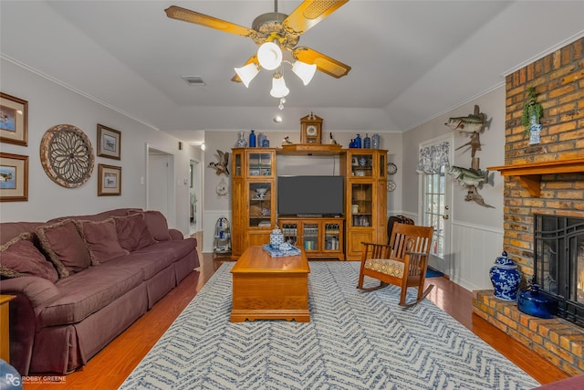 living room with ceiling fan, vaulted ceiling, a fireplace, hardwood / wood-style floors, and crown molding