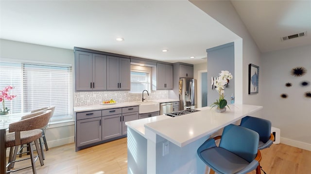 kitchen featuring a kitchen breakfast bar, gray cabinets, tasteful backsplash, light hardwood / wood-style floors, and stainless steel appliances