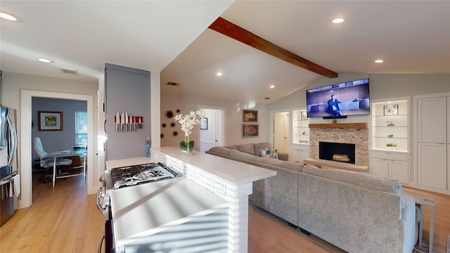 living room with a stone fireplace, built in features, light hardwood / wood-style floors, and vaulted ceiling with beams